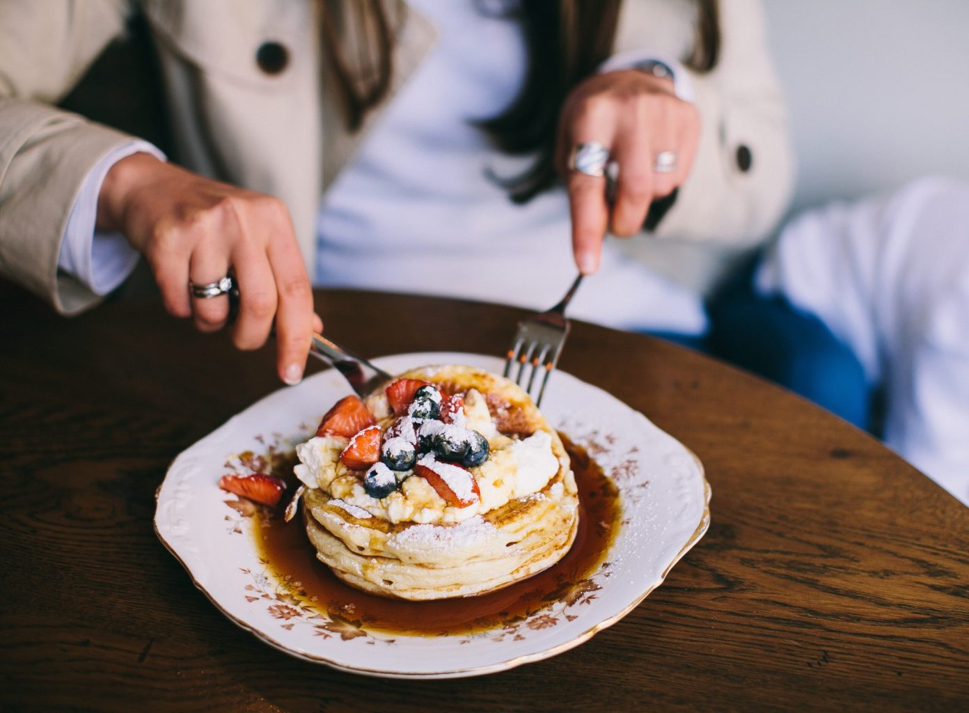 A person cutting a piece of a pancake on a plate.