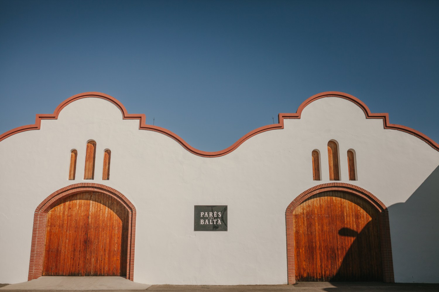 White building with two arched wooden doors and blue sky.